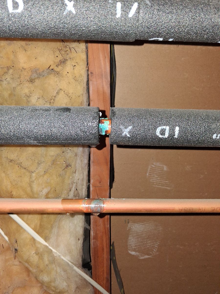 Earlier exposed hot-water piping with green corrosion visible at a gap in the insulation